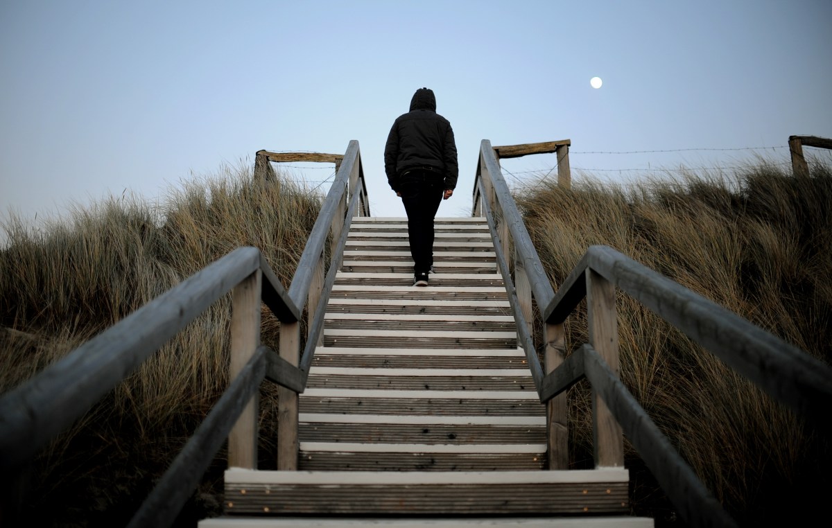 A man walks up the steps on a flight of stairs at a beach.