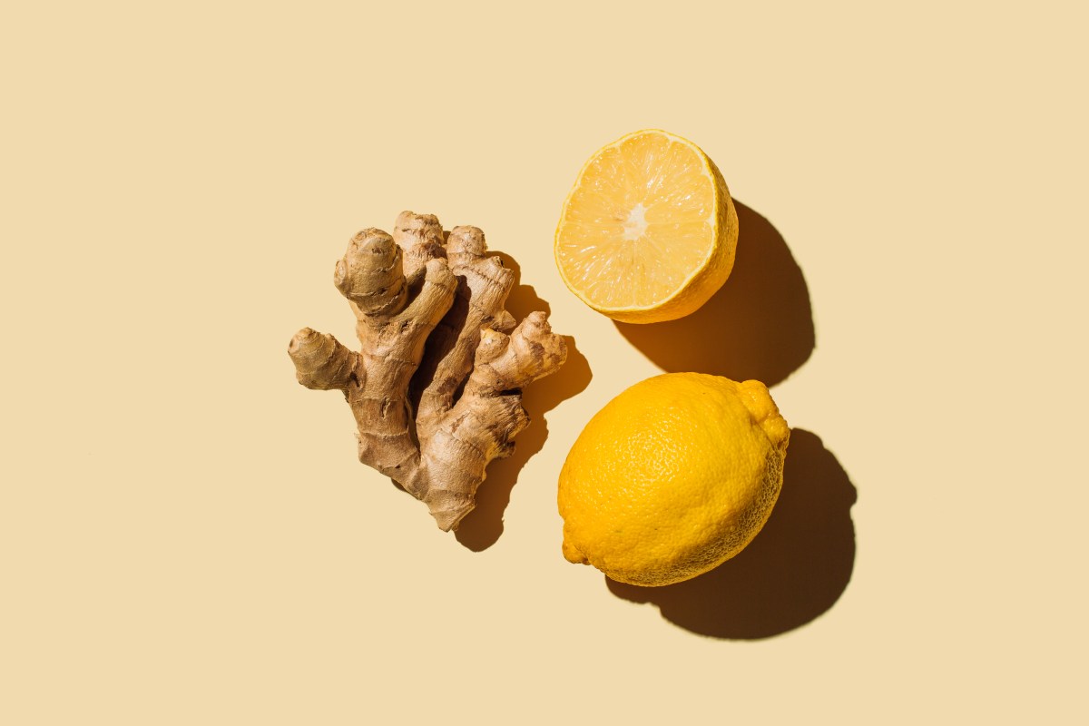 A picture of ginger root next to sliced lemons, against a yellow background.