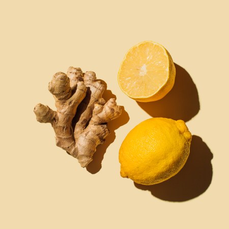 A picture of ginger root next to sliced lemons, against a yellow background.
