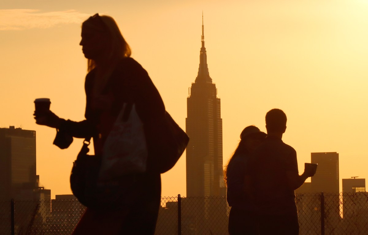 Morning commuters walk with coffees at sunrise, the Empire State Building in the background.