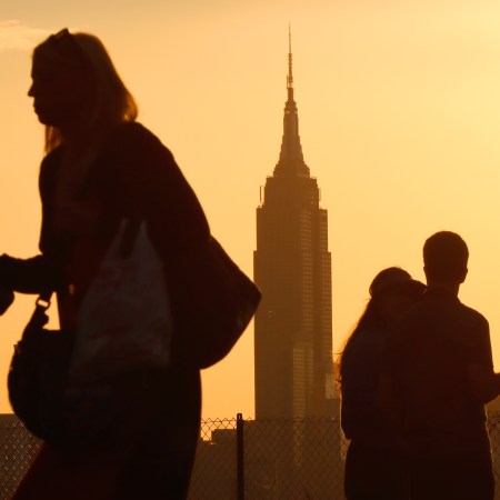 Morning commuters walk with coffees at sunrise, the Empire State Building in the background.