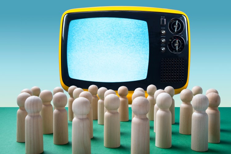Wooden figurines facing an empty old-school television.
