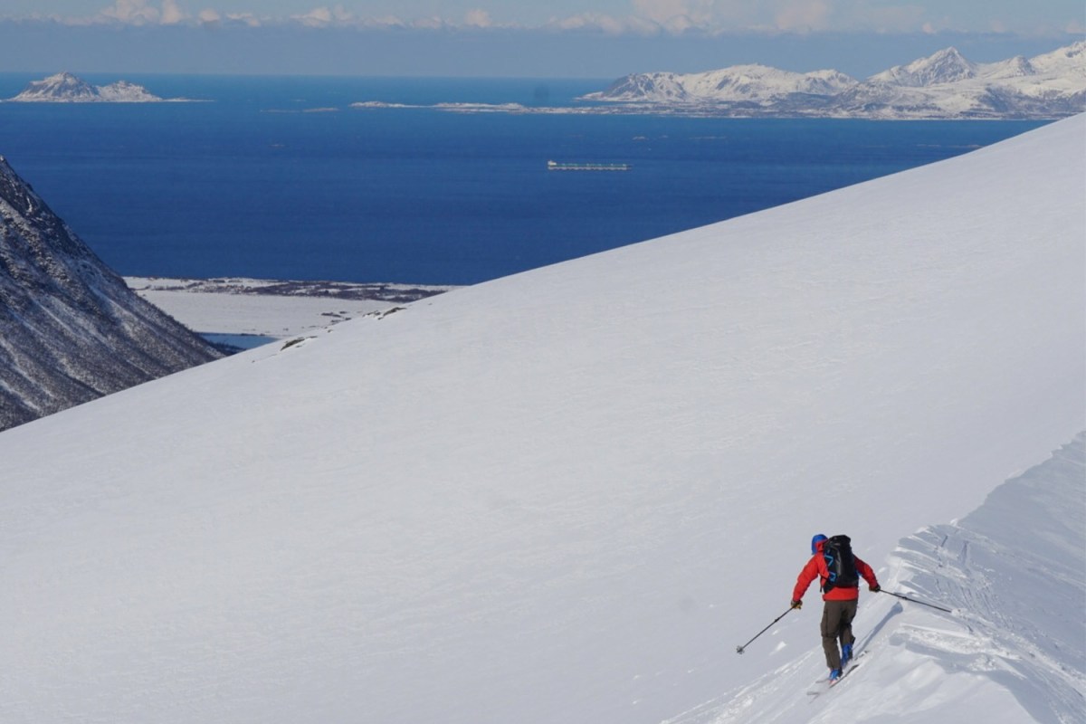 A skier on an empty mountain with the ocean in the background.