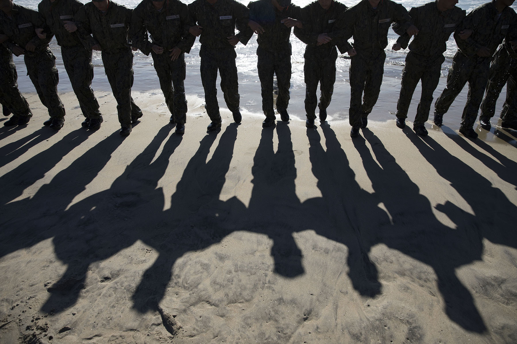 A row of Navy SEAL hopefuls standing arm in arm on a beach.