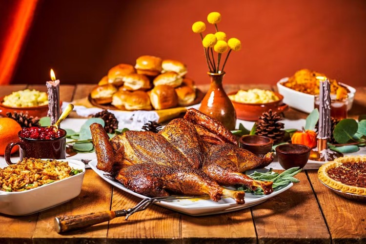 Spread of thanksgiving sides surrounded by a cooked turkey on a table