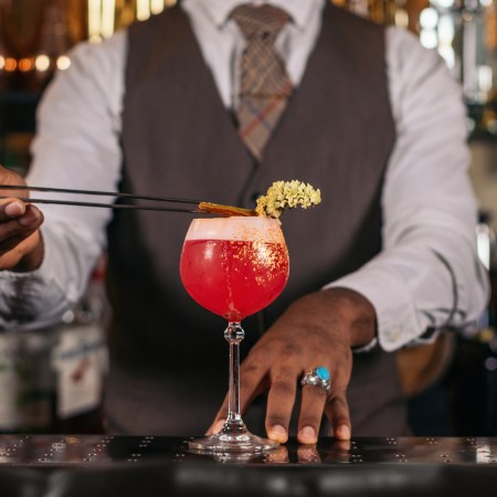 Close-up of an unrecognizable black bartender pouring a cocktail and decorating it with garnish