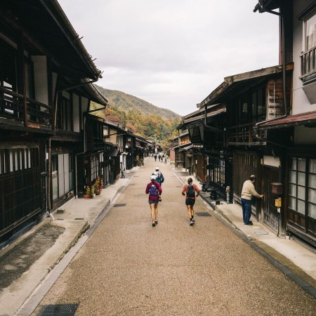 Runners on a quiet road in the Japanese Alps, running past shop keepers.