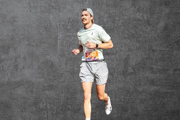 A photo of a man running in On apparel, against a grey slate background.