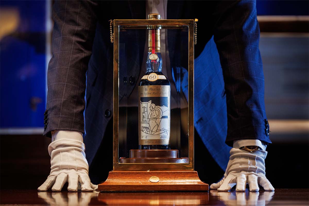 A man (neck down) standing over a bottle of The Macallan Adami 1926, which just broke a spirits auction record