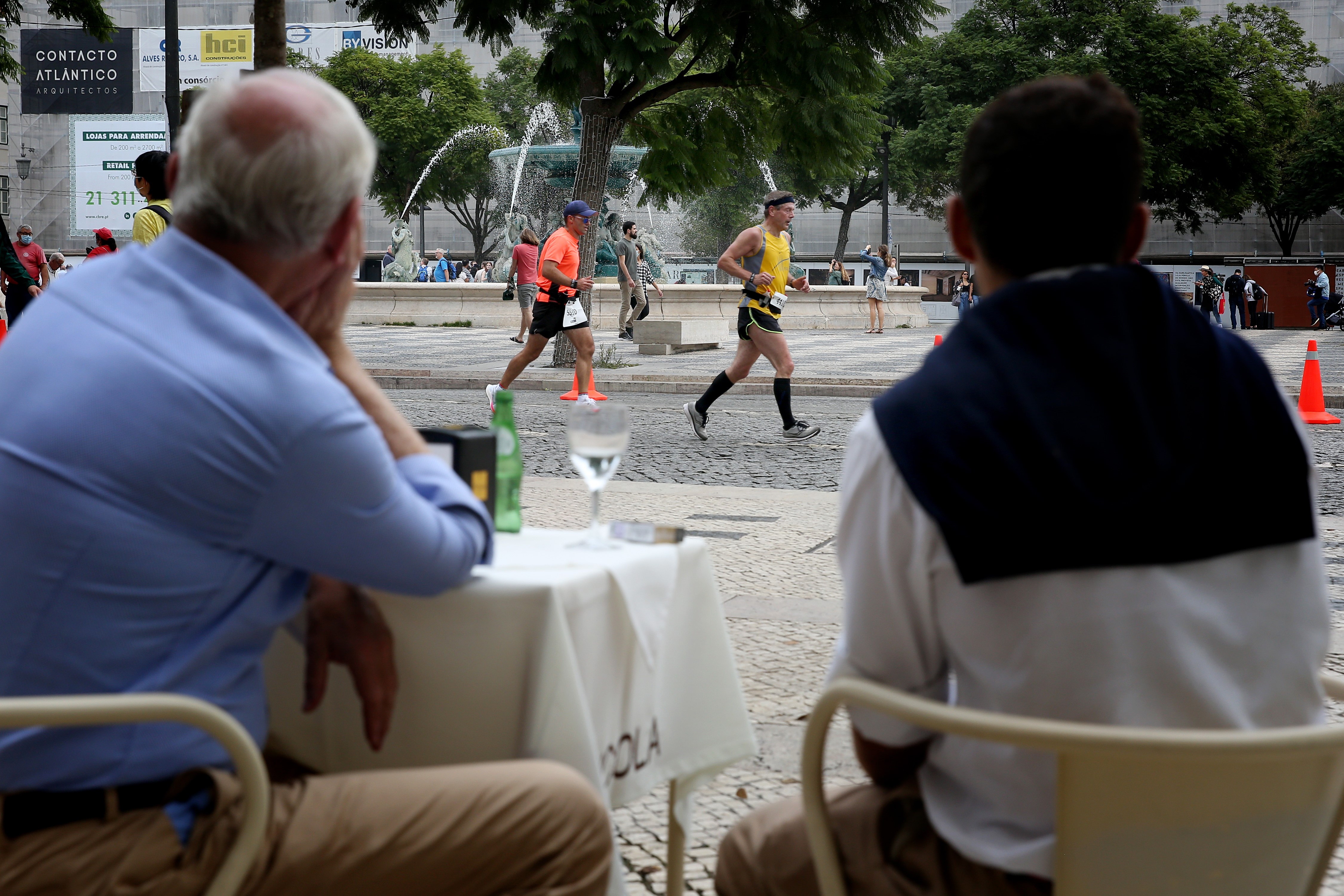 Two men sharing drinks watch runners race down cobblestoned streets in Lisbon, Portugal.