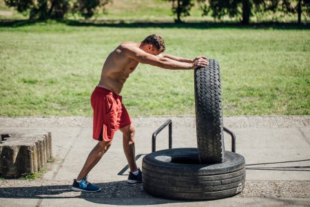 A shirtless man flipping a tire.