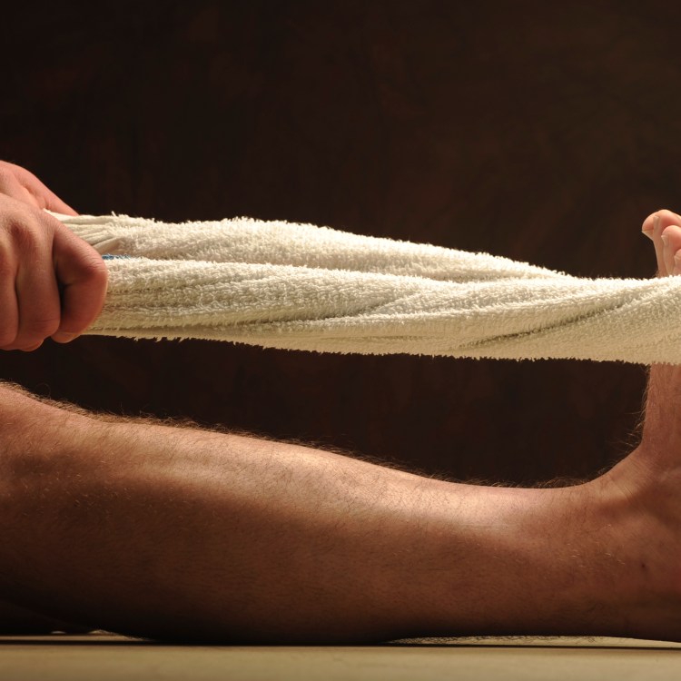 A person stretching their legs with a towel. Working out with a towel is surprisingly effective.