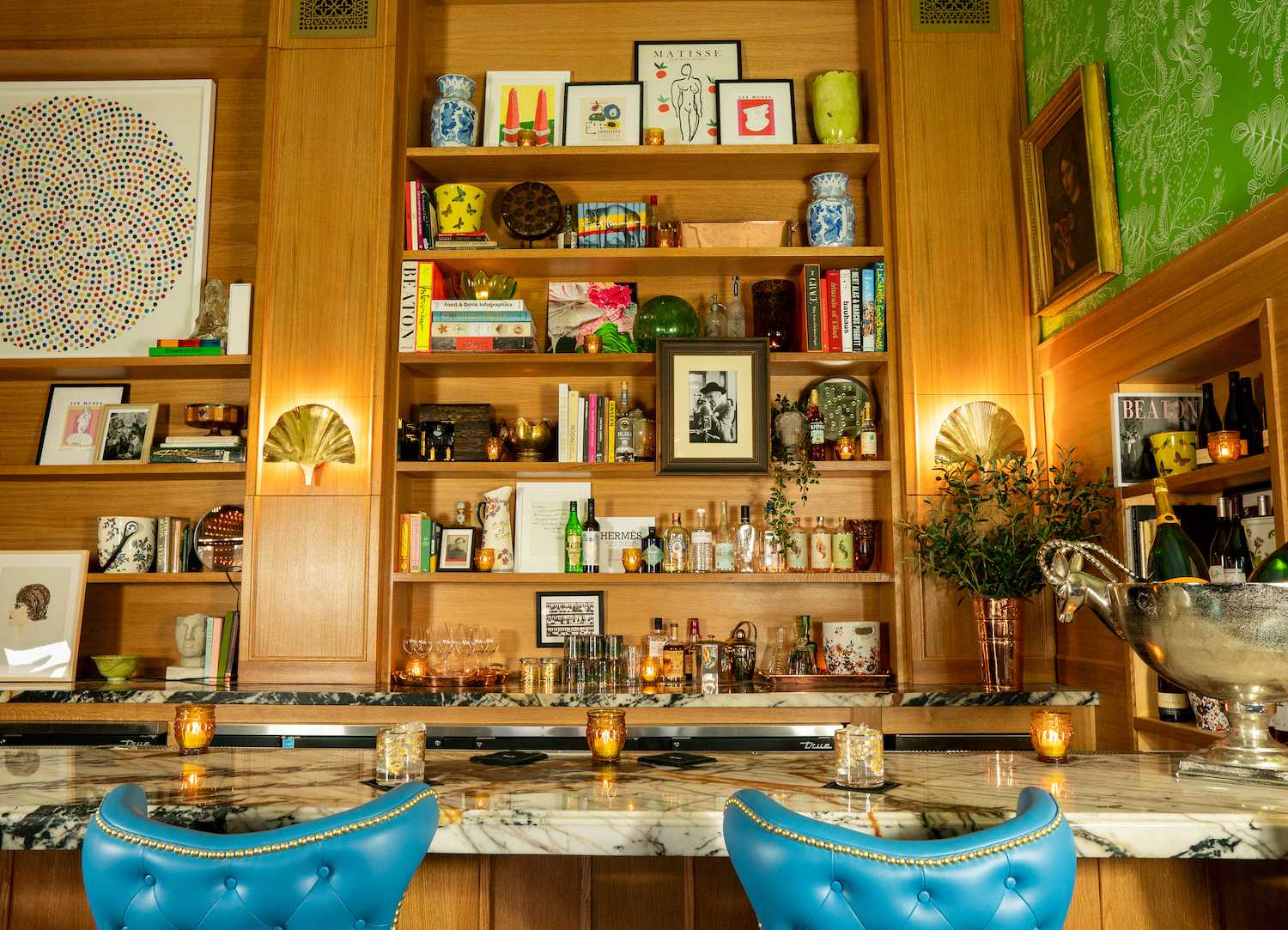 Marble bar with bright blue chairs and shelves with art and bottles of various spirits