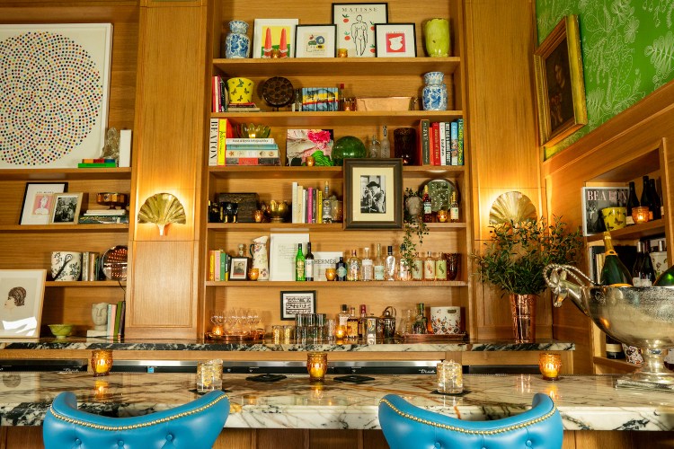 Marble bar with bright blue chairs and shelves with art and bottles of various spirits
