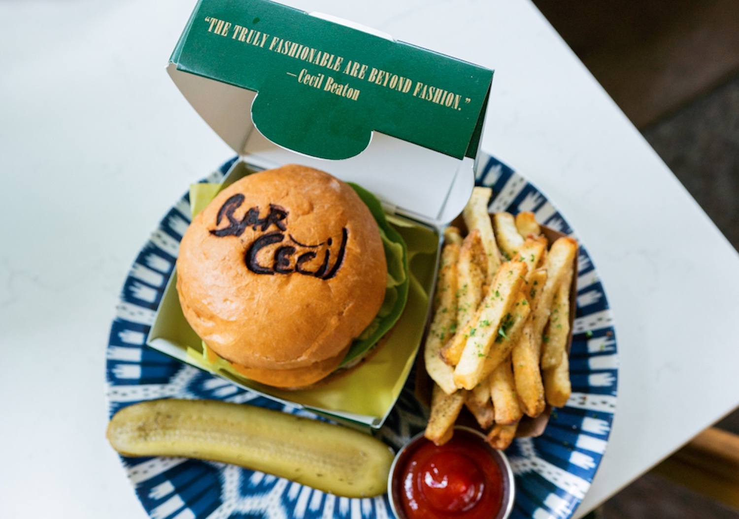 Bar Cecil's Beaton Burger, with the name "Bar Cecil" burnt into the top of the bun, with a side of fries and a pickle 