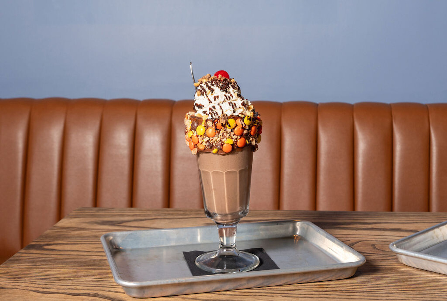 Chocolcate shake in a glass rimmed with Reeses Pieces and topped with whipped cream, chocolate sauce and a cherry