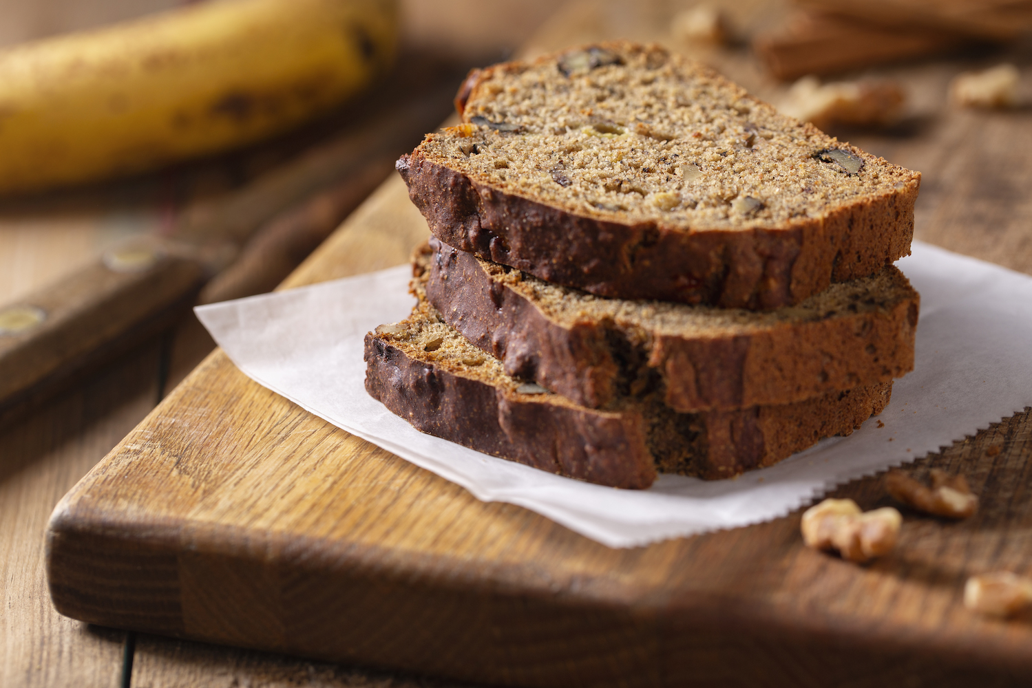 Slices of fresh baked banana nut bread with walnuts on rustic wood cutting board