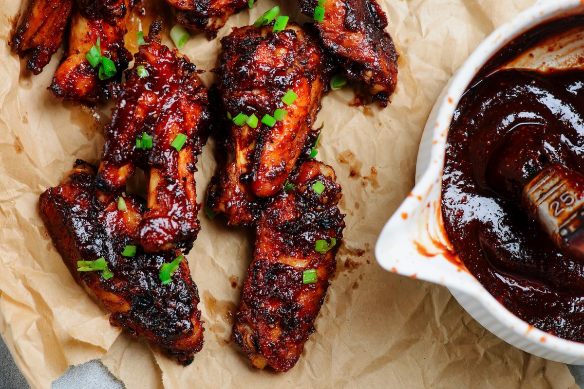 barbecue chicken wings on parchment next to a bowl of barbecue sauce
