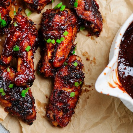 barbecue chicken wings on parchment next to a bowl of barbecue sauce