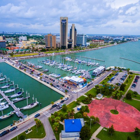 Corpus Christi Texas Aerial Over Marina With a Circle pattern on the T-head and Sailboats and Yatch's on the marina on an amazing day with the CCTX skyline cityscape background and the Harbor Bridge in the distance. Coastal Small Town Paradise vibe.
