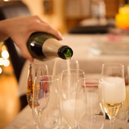 Adult pouring champagne into drinking glasses at a house party