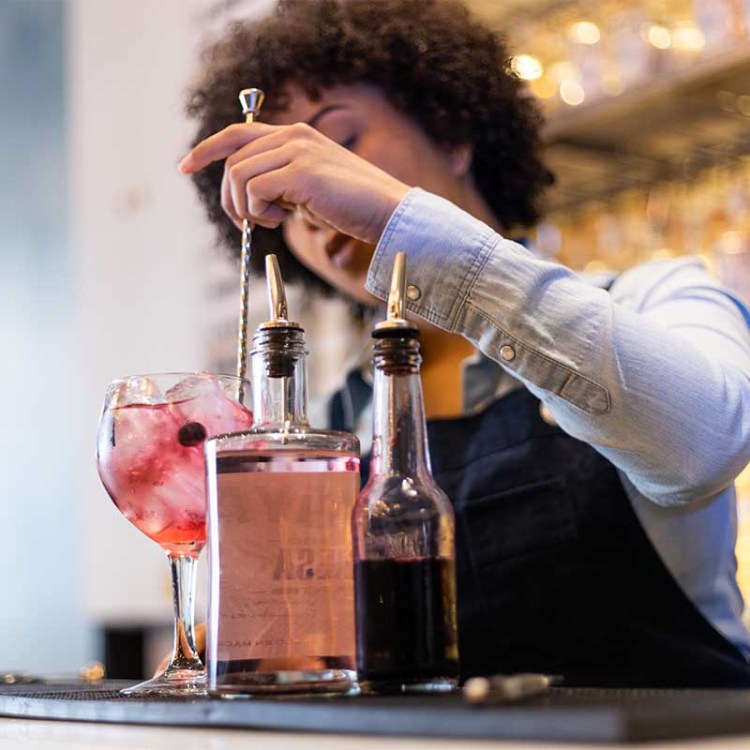 A woman preparing cocktails behind a bar, front view. Bacardi's latest Cocktail Trends Report suggests what we'll be consuming in 2024.