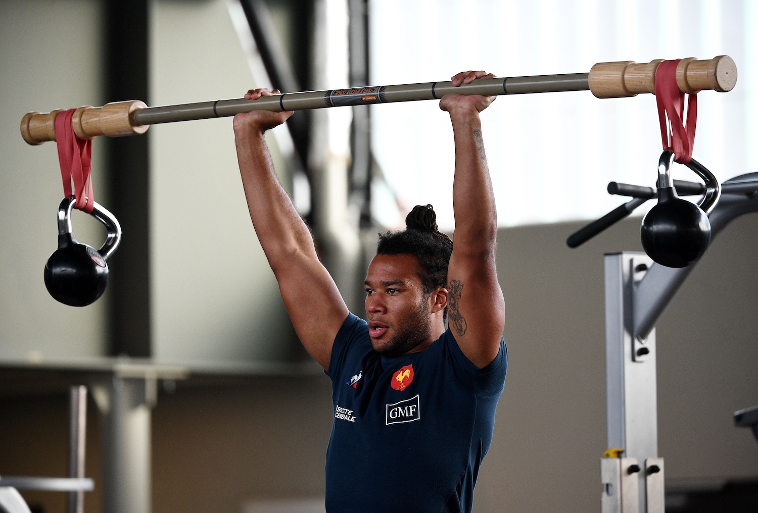 A man in a gym lifting a barbell with a kettlebell attached. This is what's known as chaos training.