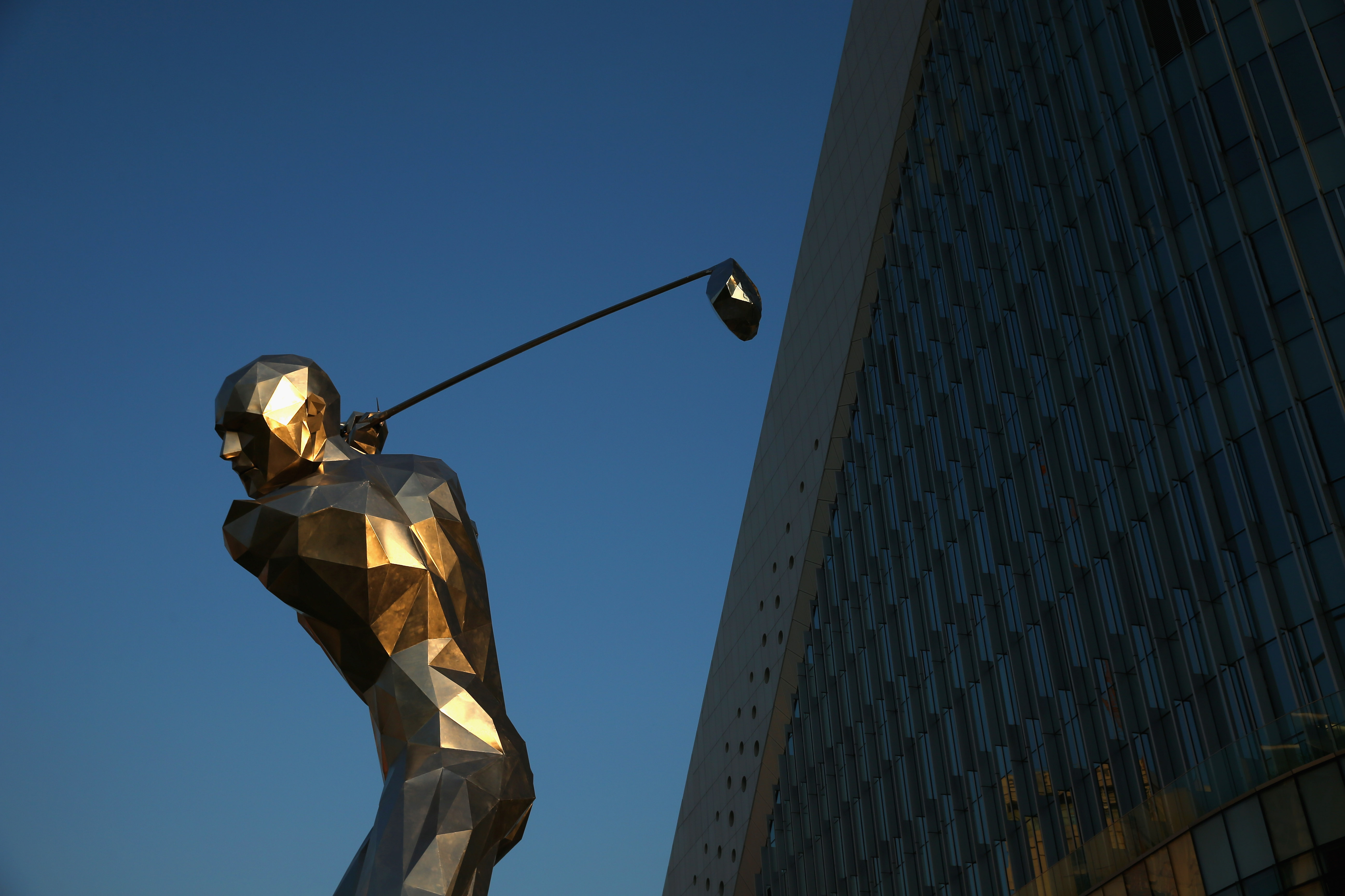 A statue of a golfer outside a futuristic office building.