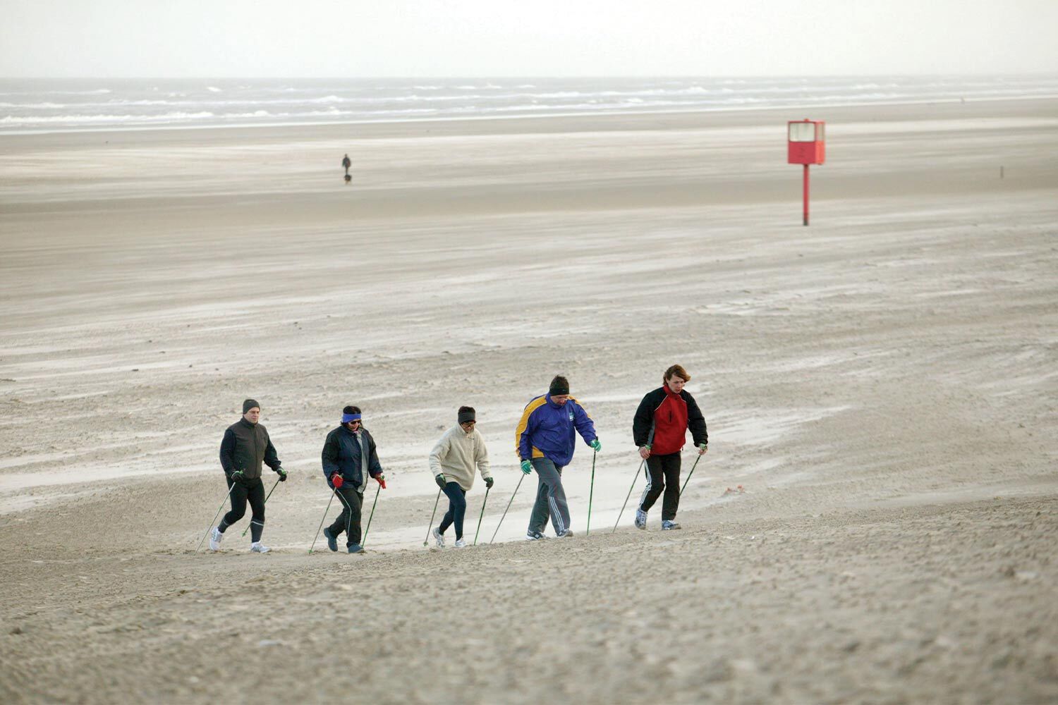 A group of adults Nordic walking across a cold beach.