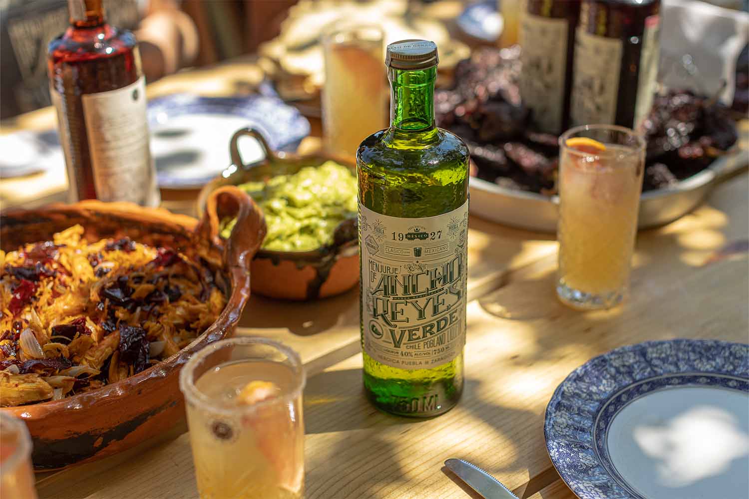 Ancho Reyes Verde on a table with food and cocktails