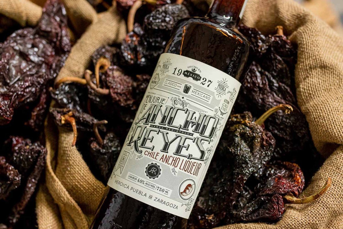 A bottle of Ancho Reyes Original liqueur on a bed of chiles