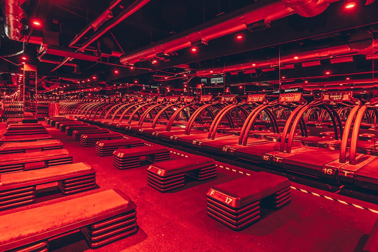 Interior of Barry's with treadmills and other workout equipment in mirrored room with dim red lights 