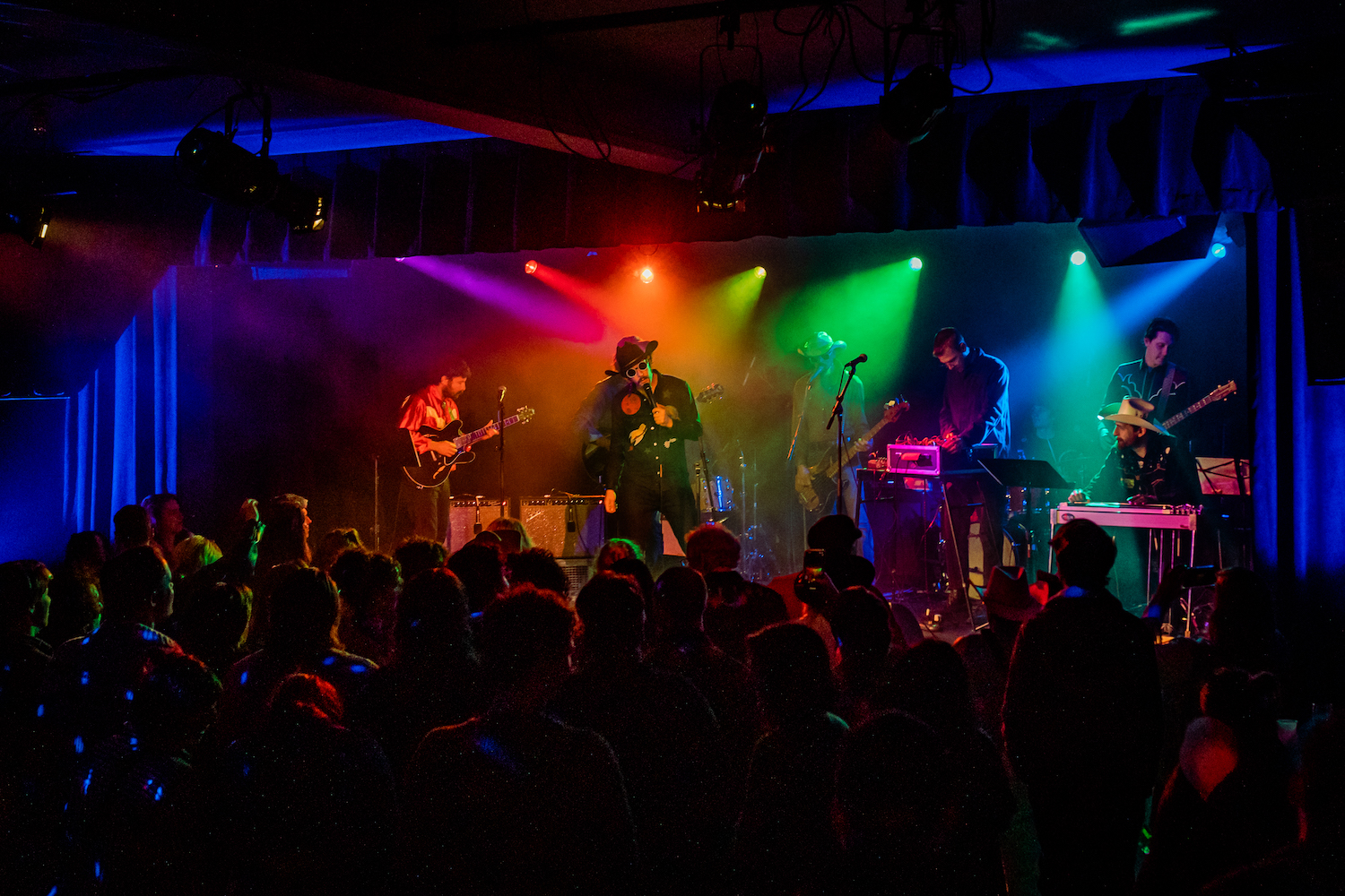 Band members on a stage performing dressed as cowboys with mutlti-colored strobe lights 
