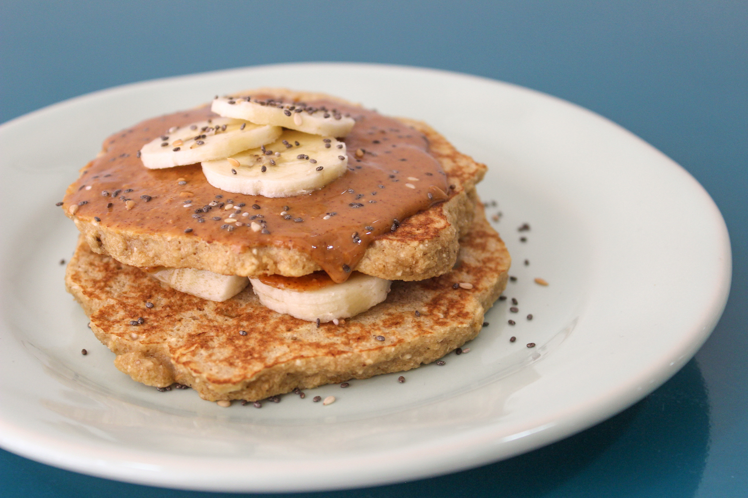 Oat pancakes with peanut butter, chia seeds and banana on a white plate