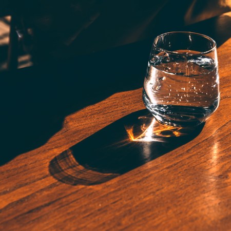 A glass of sparkling water standing on a sunlit wooden table casting shadows and lens flare