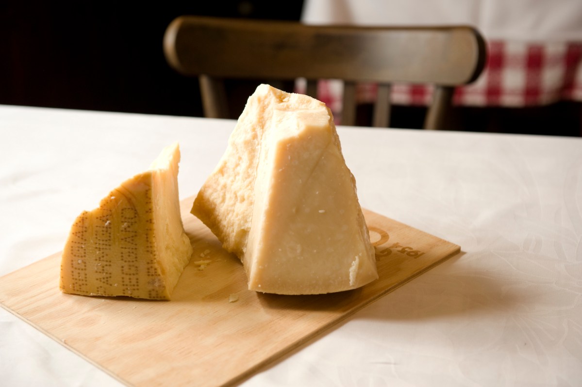 two large pieces of parmigiano reggiano cheese on a wooden board on a white table