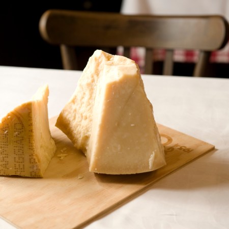 two large pieces of parmigiano reggiano cheese on a wooden board on a white table