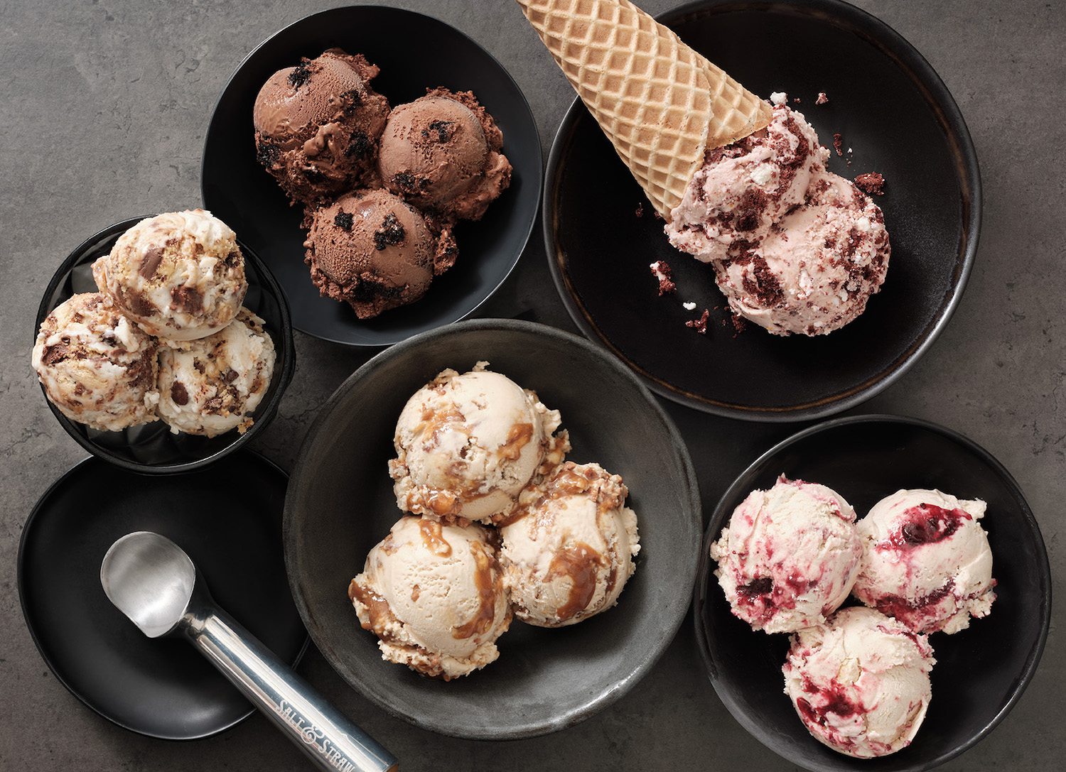 Scoops of ice cream in a bowl with a cone and an ice cream scoop from a birds-eye view