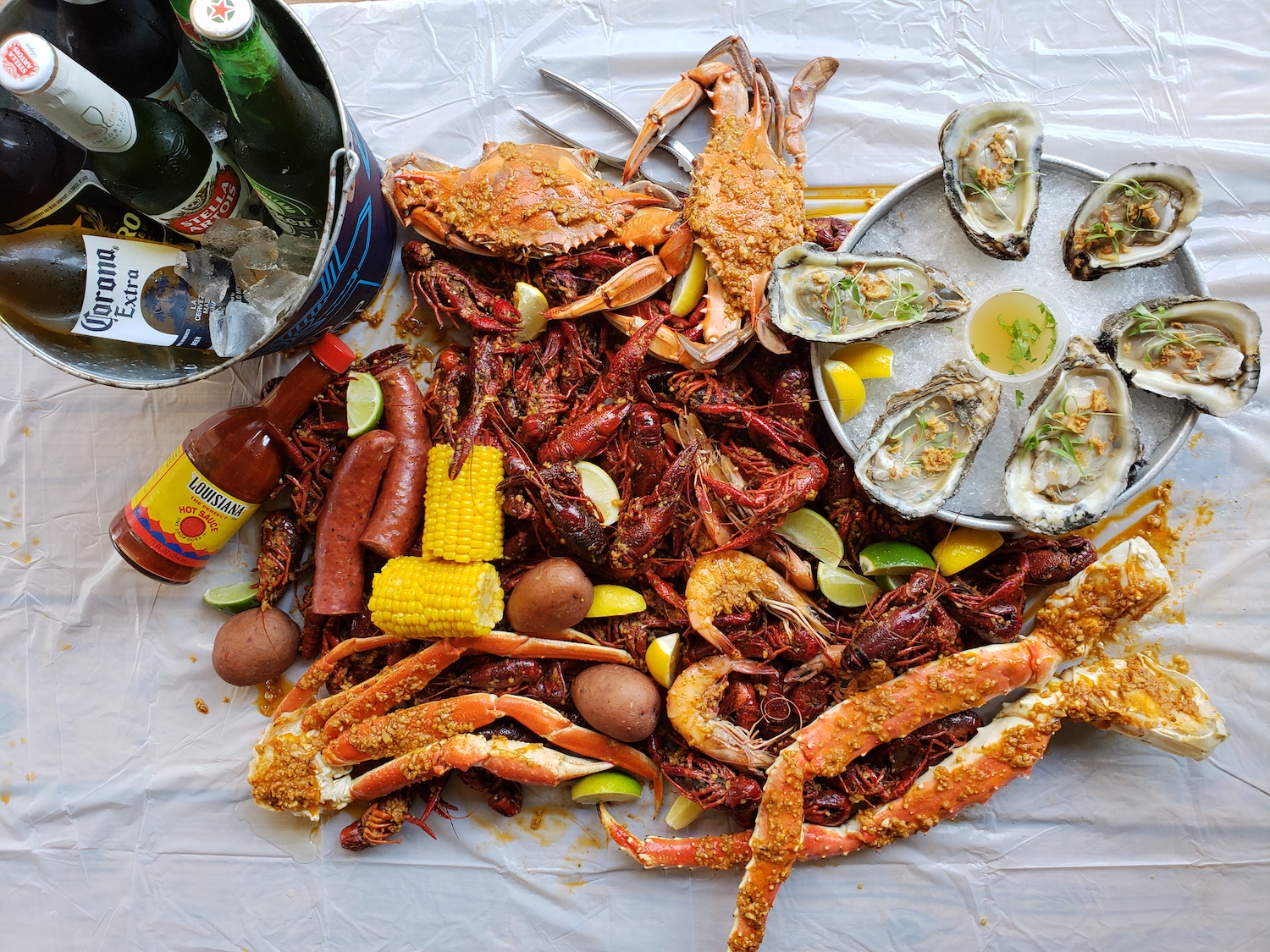 Crawfish, shrimp, crab, oysters, potatoes, corn and beer in a pile 