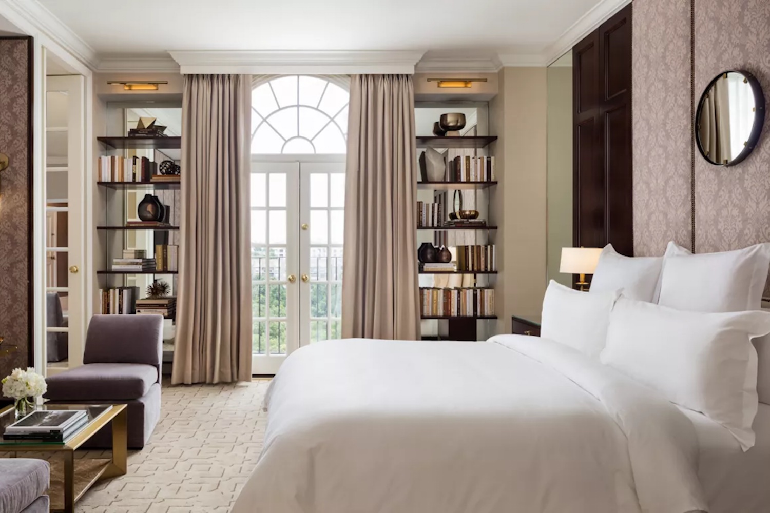 Bedroom in Rosewood Mansion with white bedding and bookshelves with doorway to terrace and small seating area