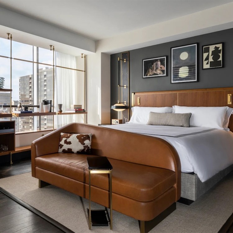 Bedroom in Thompson Dallas with brown leather bedframe, white bedding, floor-to-ceiling window view of city and high quality room accents