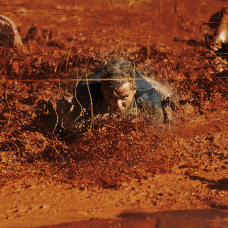 An image of men crawling through mud under live wires during a Tough Mudder event. We take a look at what happened to the king of obstacle course races.
