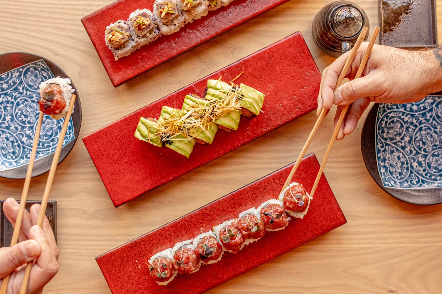 Spread of sushi on plates with people picking them up with chopsticks 