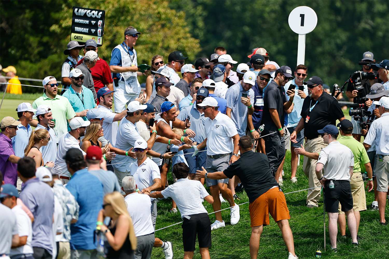 A LIV Golf player high-fives fans on the side of the course.
