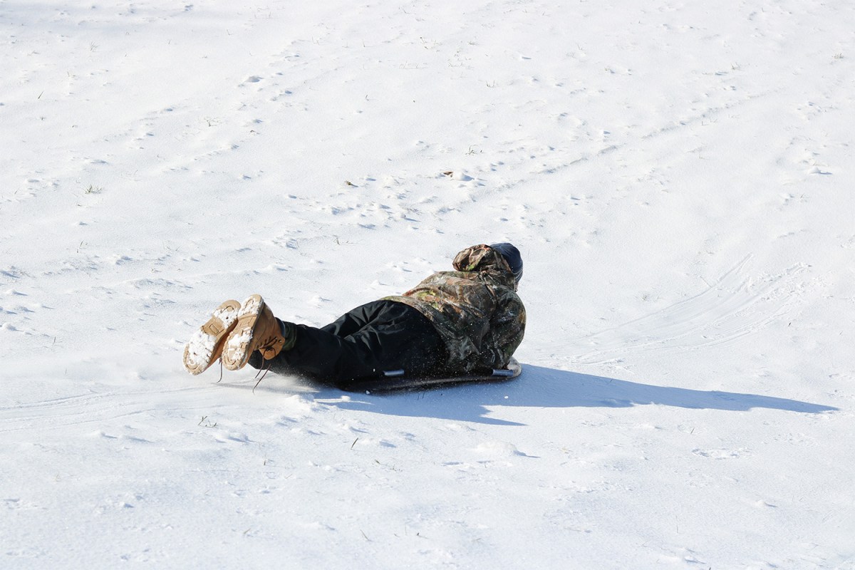 An adult in a camo winter jacket sledding down a hill.