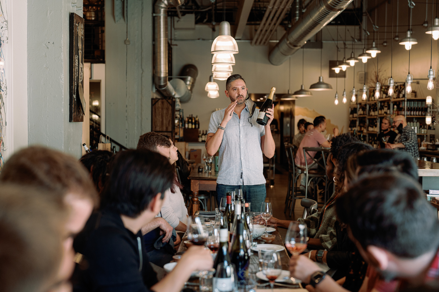 a man holding a wine bottle and conducting a tasting with a table of people