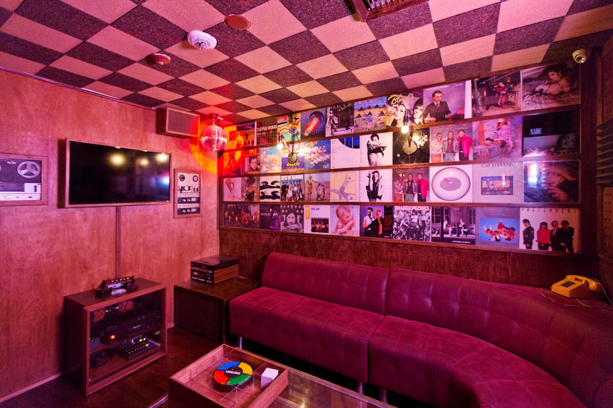 Karaoke room in Break Room 86 with large booth seat, artwork on walls and colored lighting