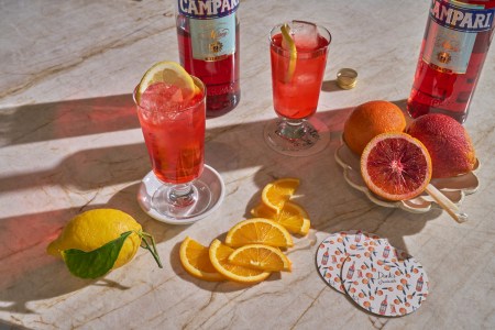 Beverages in glasses surrounding a bottle of Campari and other garnishes