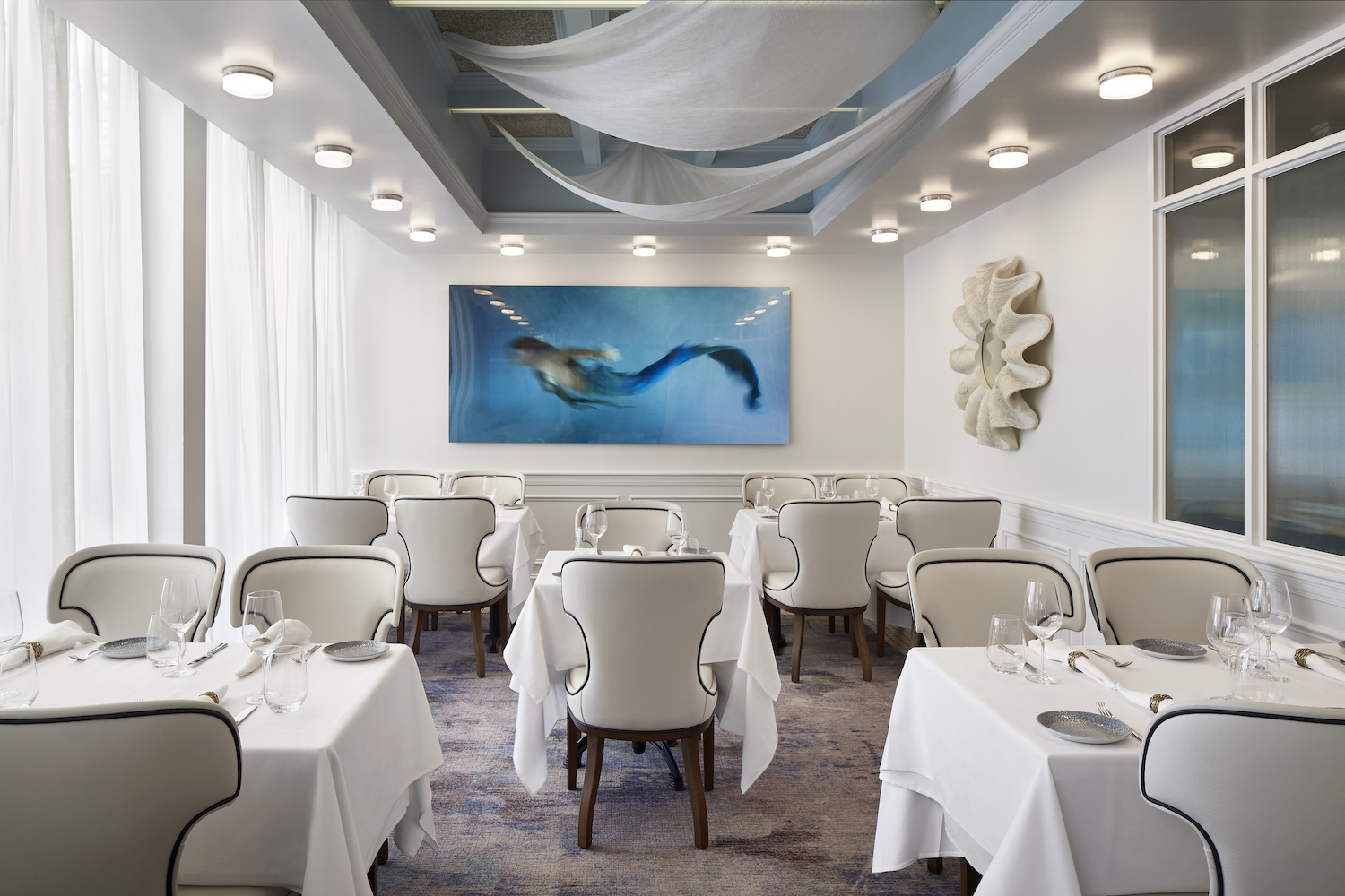 White accented dining area with tables, couch chairs and a mermaid painting on the wall