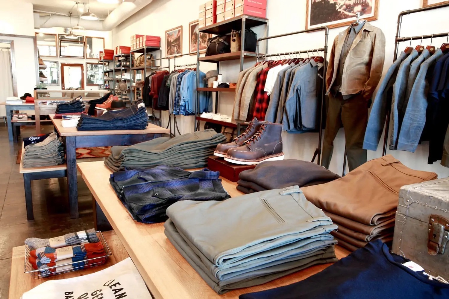 Interior of General Quarters with jeans, shirts and boots folded on display tables with clothes hanging on a rack behind them